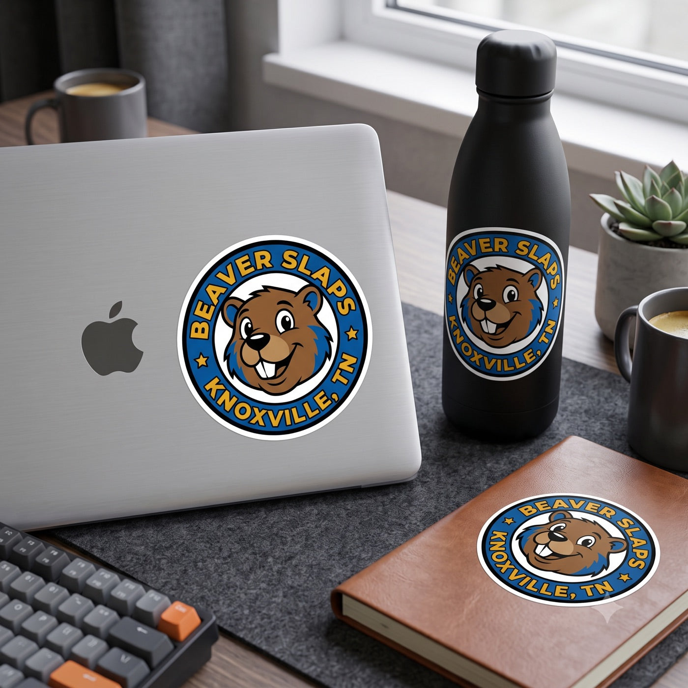 Beaver Slaps round badge sticker on a laptop, water bottle, and journal